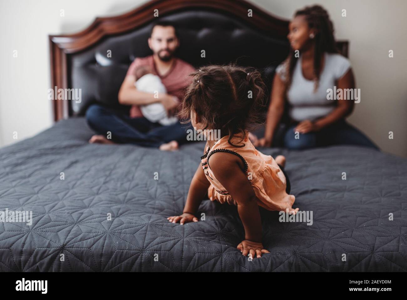 In Fokus gemischtrassigen Mädchen auf dem Bett zurück an blurry Familie Stockfoto