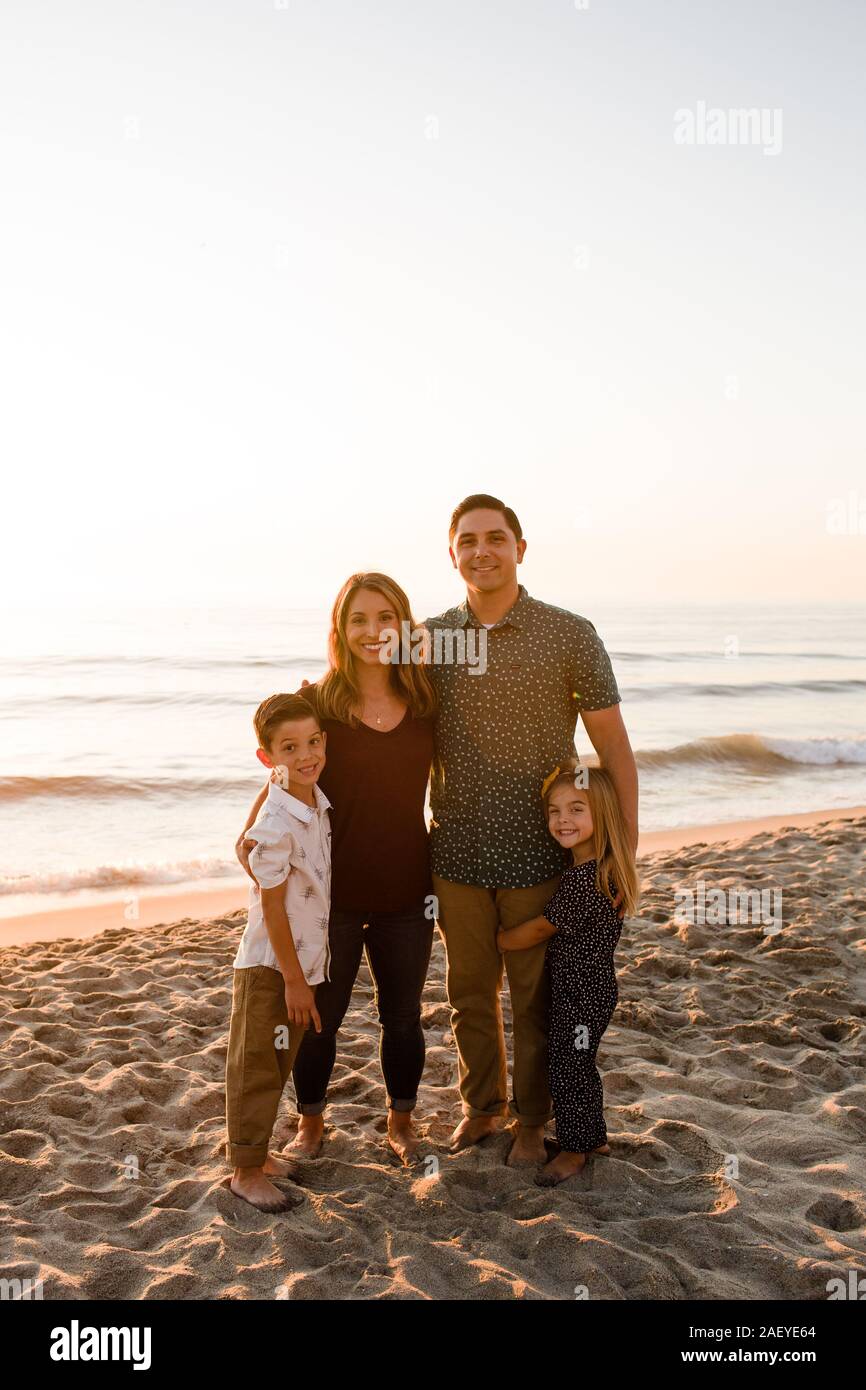 Familie von vier Lächeln auf die Kamera, die am Strand bei Sonnenuntergang Stockfoto