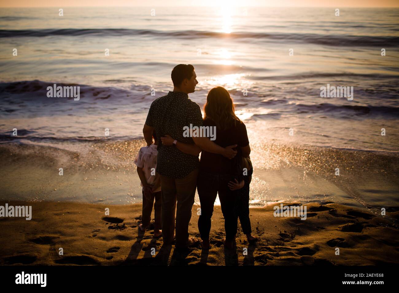 Familie von vier Ständigen am Strand, am Meer bei Sonnenuntergang Stockfoto