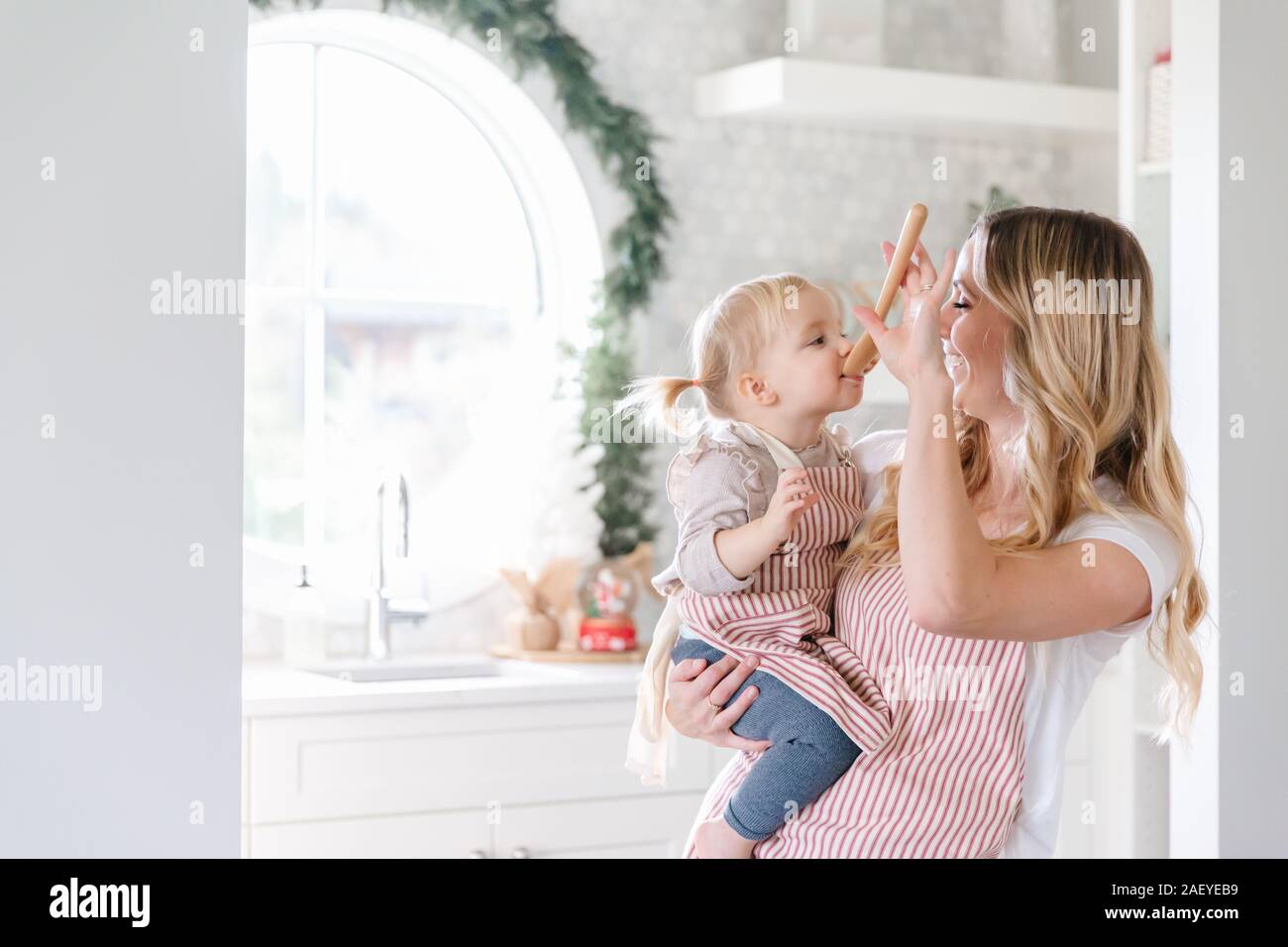 Mutter Holding baby Tochter in passenden Schürzen backen in der Küche Stockfoto