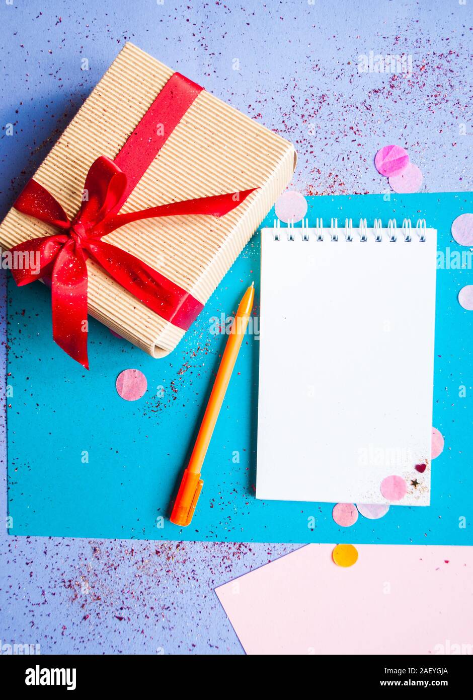 Geschenkset verbeugte sich mit roter Schleife auf lila Hintergrund mit bunten Konfetti, Geschenkset, Pen und Notebook. Vorsätze im Neuen Jahr Konzept. Stockfoto