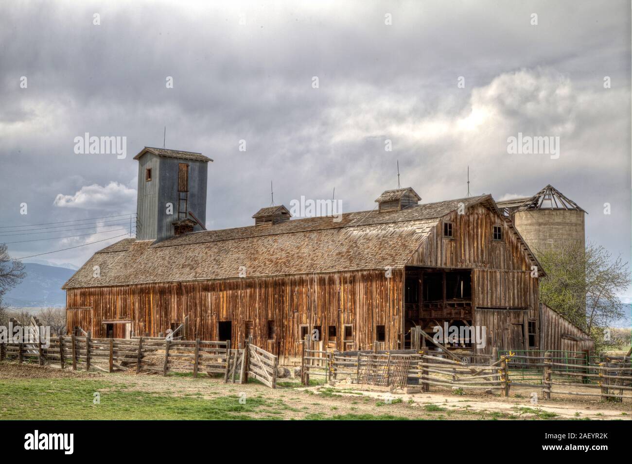 Eine rustikale Scheune durch eine ebenso Wetter abgenutzte Holz Zaun und von einem obdachlosen Silo begleitet umgeben. Stockfoto