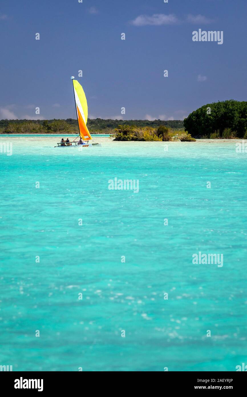 Ein farbenfrohes Segelboot und das azurblaue Wasser des „Sees of Seven Blues“ in Bacalar, Quintana Roo, Mexiko. Stockfoto