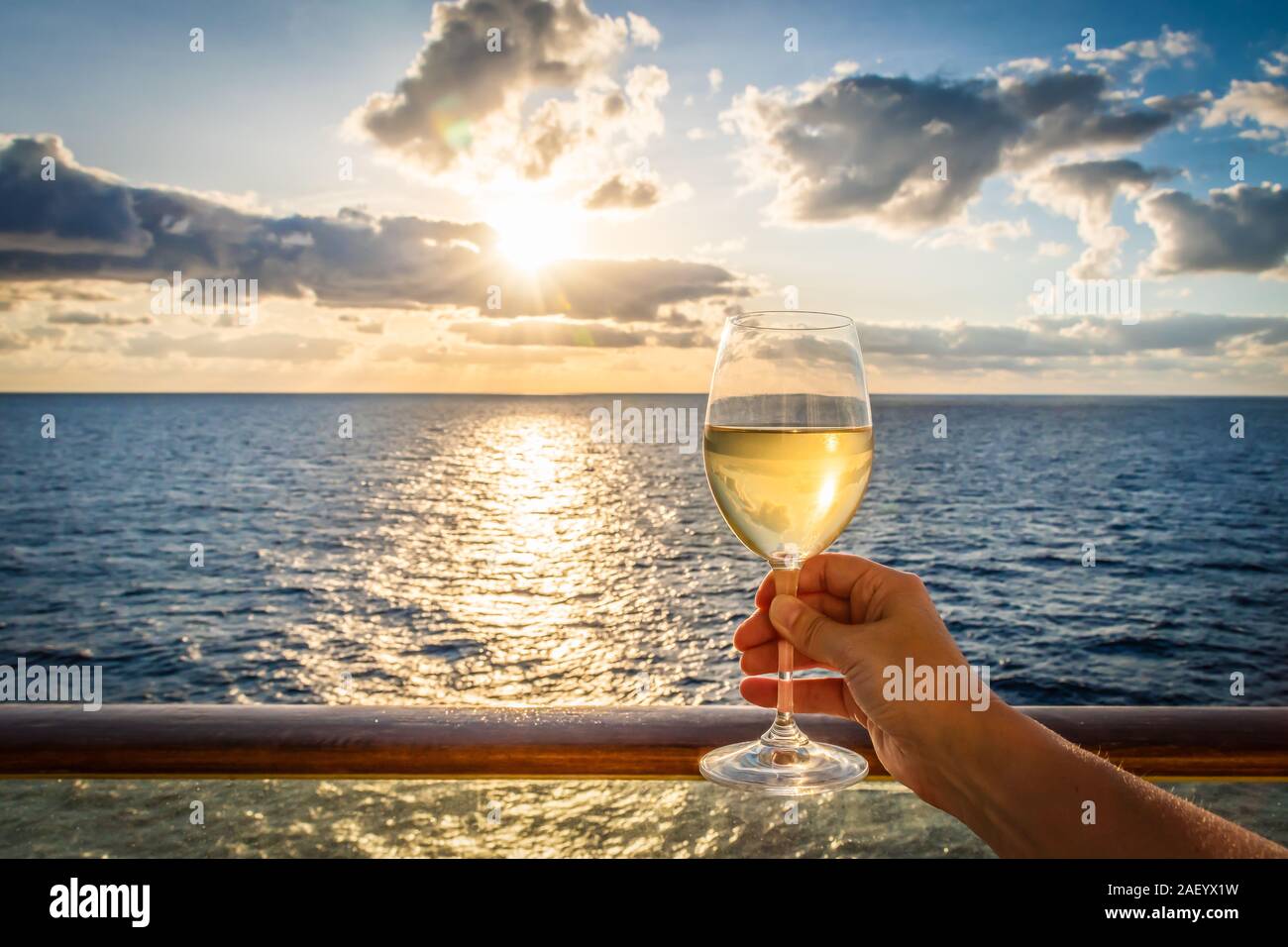 Bei Sonnenuntergang eine weibliche Hand Toast das Neue Jahr mit einem Glas Weisswein. Foto auf einem Balkon eines Kreuzfahrtschiffes mit Meerblick genommen. Stockfoto