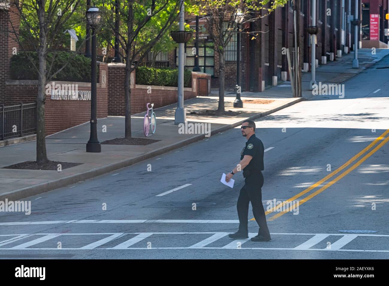 Atlanta, USA - 20. April 2018: Mann Polizist Polizist beim Zebrastreifen überqueren der Straße in der Innenstadt von Stadt mit öffentlichen Schulgebäude Stockfoto