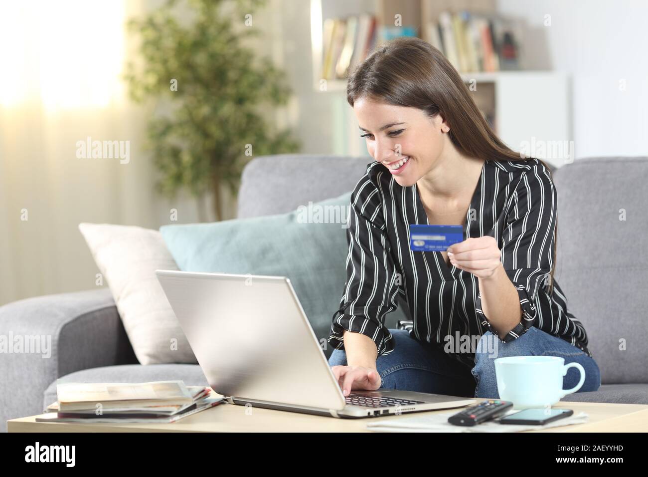 Glückliche Frau kaufen on-line mittels Laptop und Kreditkarte auf einer Couch im Wohnzimmer zu Hause sitzen Stockfoto