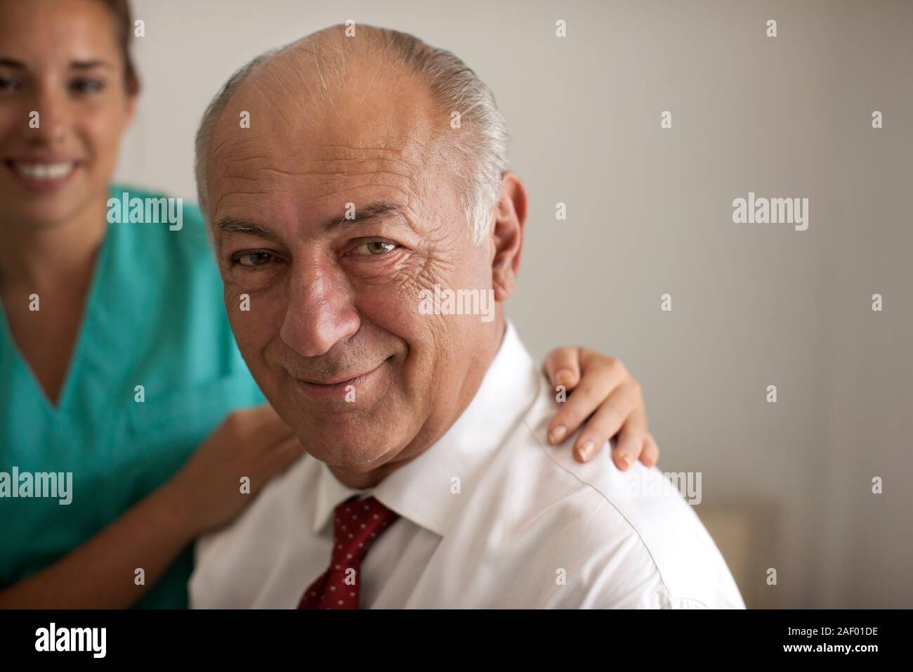 Junge Krankenschwester mit ihren Händen auf den Schultern eines älteren männlichen Patienten. Stockfoto