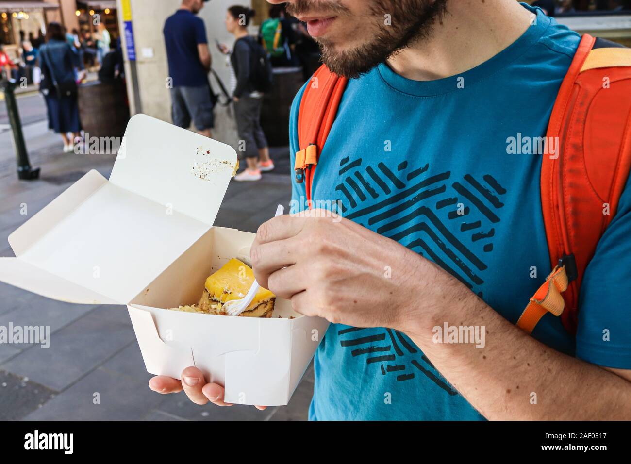 Junge mit Bart Kuchen essen mit Kunststoff Gabel in einem Papier essen Container in Borough Market London Stockfoto