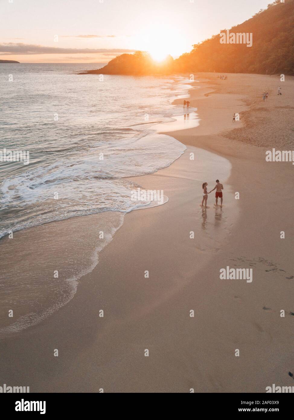 Ein Paar, das seine Flitterwochen verbringt, an einem Strand auf hawaii entlang läuft, während es den Sonnenuntergang genießt Stockfoto