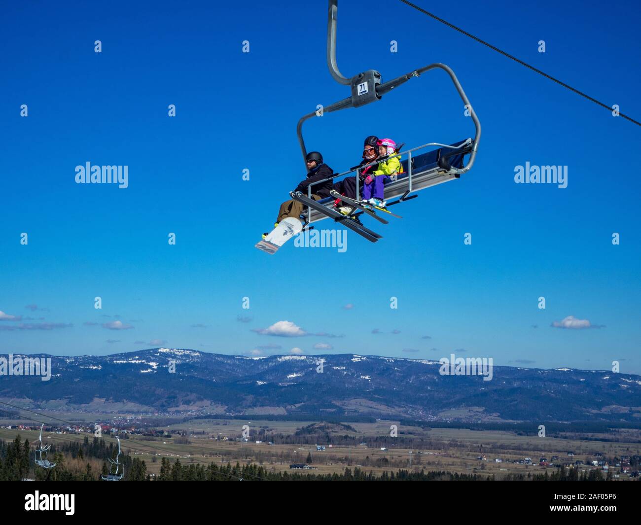 Bialka Tatrzanska, Polen - 27. März 2018: ein Sessellift auf blauen Himmel mit einem Snowboarder und Skifahrer: eine Frau und ein Kind in einem gelben Skijacke, Viole Stockfoto