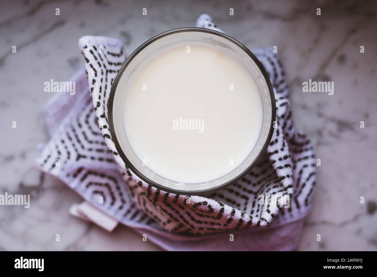 Blick von oben auf die heiße Milch in einem Glas in Tuch eingewickelt und auf weißem Marmor Tisch gelegt. Darstellung der Self-care Idee. Stockfoto