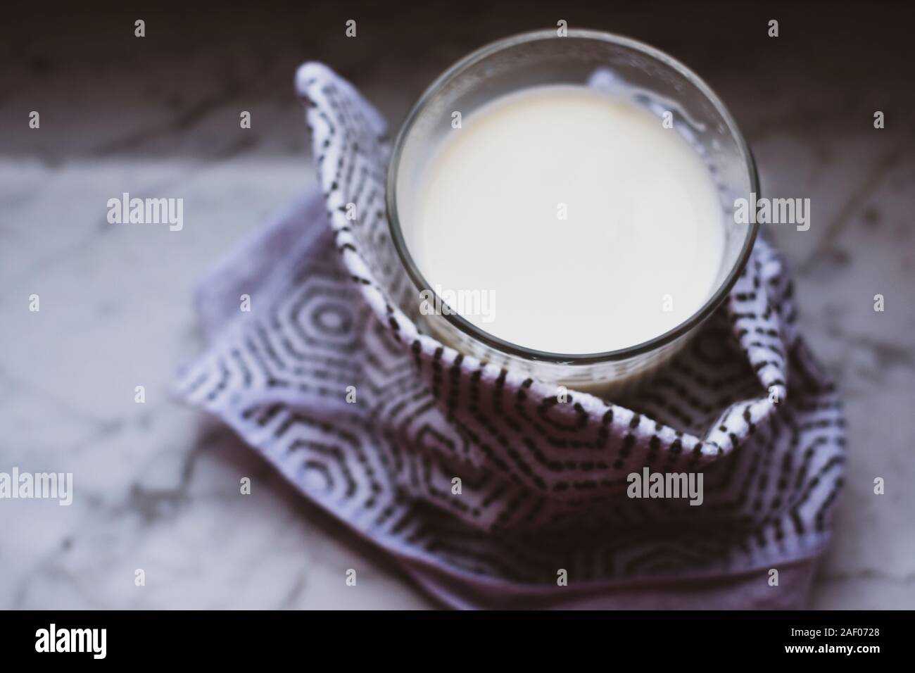 Blick von oben auf die heiße Milch in einem Glas in Tuch eingewickelt und auf weißem Marmor Tisch gelegt. Darstellung der Self-care Idee. Stockfoto