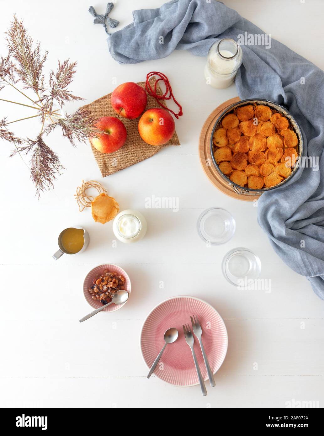 Weiße Holztisch mit Apple Brot und Butter Pudding, jar mit saurer Sahne, Glas Milch, Hintergrund mit ein paar Äpfel und Vase mit trockenen gra eingerichtet Stockfoto