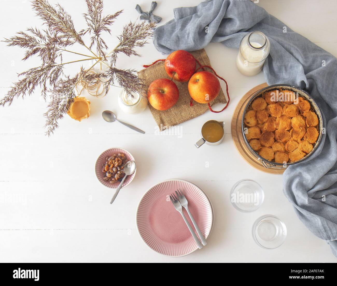 Weiße Holztisch mit Apple Brot und Butter Pudding, jar mit saurer Sahne, Glas Milch, Hintergrund mit ein paar Äpfel und Vase mit trockenen gra eingerichtet Stockfoto