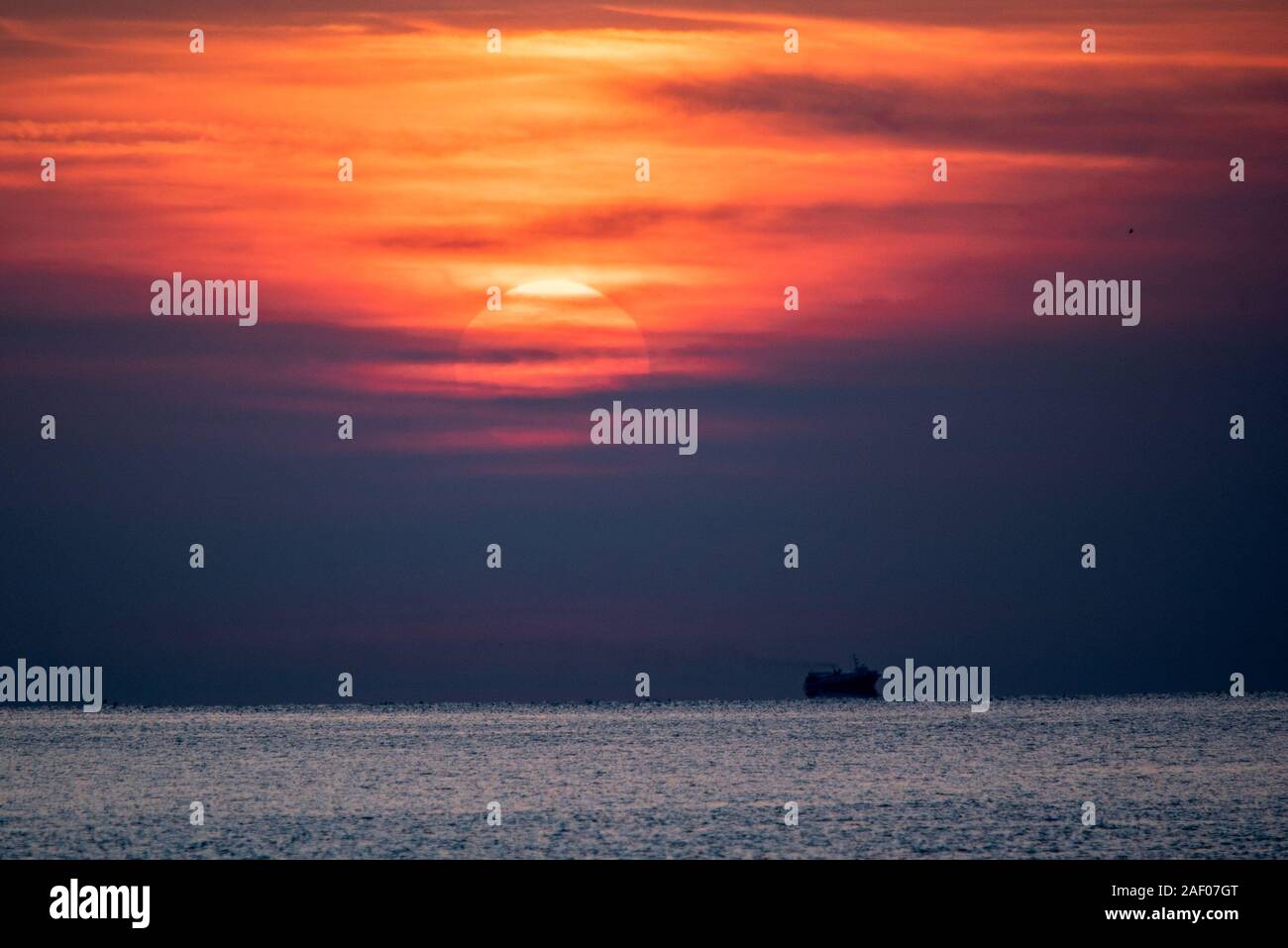 Sonnenuntergang Szene am Meer. Dramatische Roter Himmel über der Silhouette eines Schiffes in ruhigen Meer. Stockfoto