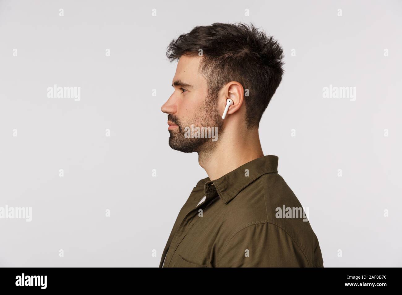 Close-up Profil Schuß gut aussehender bärtiger junger Mann im Mantel, tragen, drahtlose Kopfhörer, zu Fuß oder in der U-Bahn, schöne Sound Qualität, Stockfoto