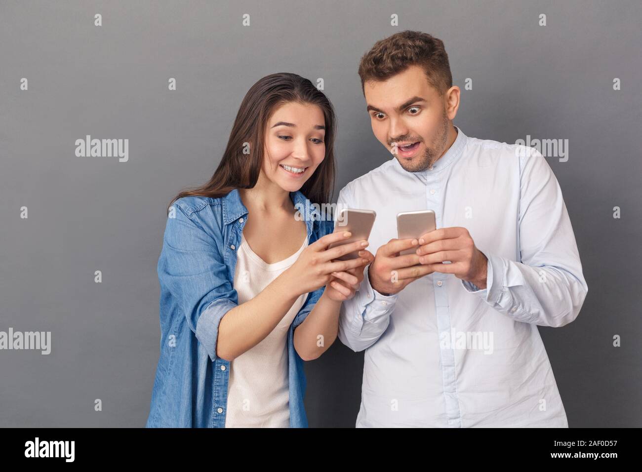 Zur Verwendung der Geräte. Junges Paar Studio stehen isoliert auf Grau mit jeder anderen Medien auf dem Smartphone Lächeln aufgeregt Stockfoto