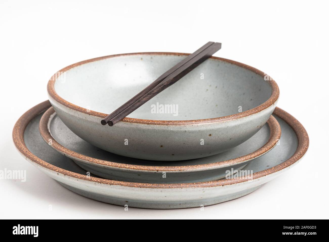 Ein paar orientalische schwarze hölzerne Stäbchen ruht auf einem Abendessen von texturierten Steinzeug Platten auf weißem Hintergrund. Stockfoto
