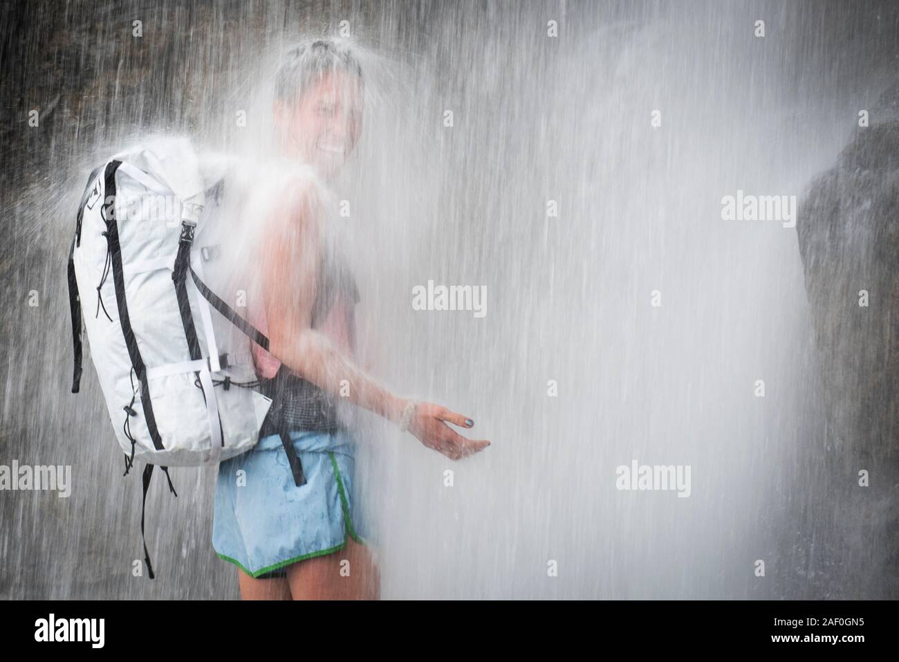 Lachende Frau, die unter Wasserfall Stockfoto