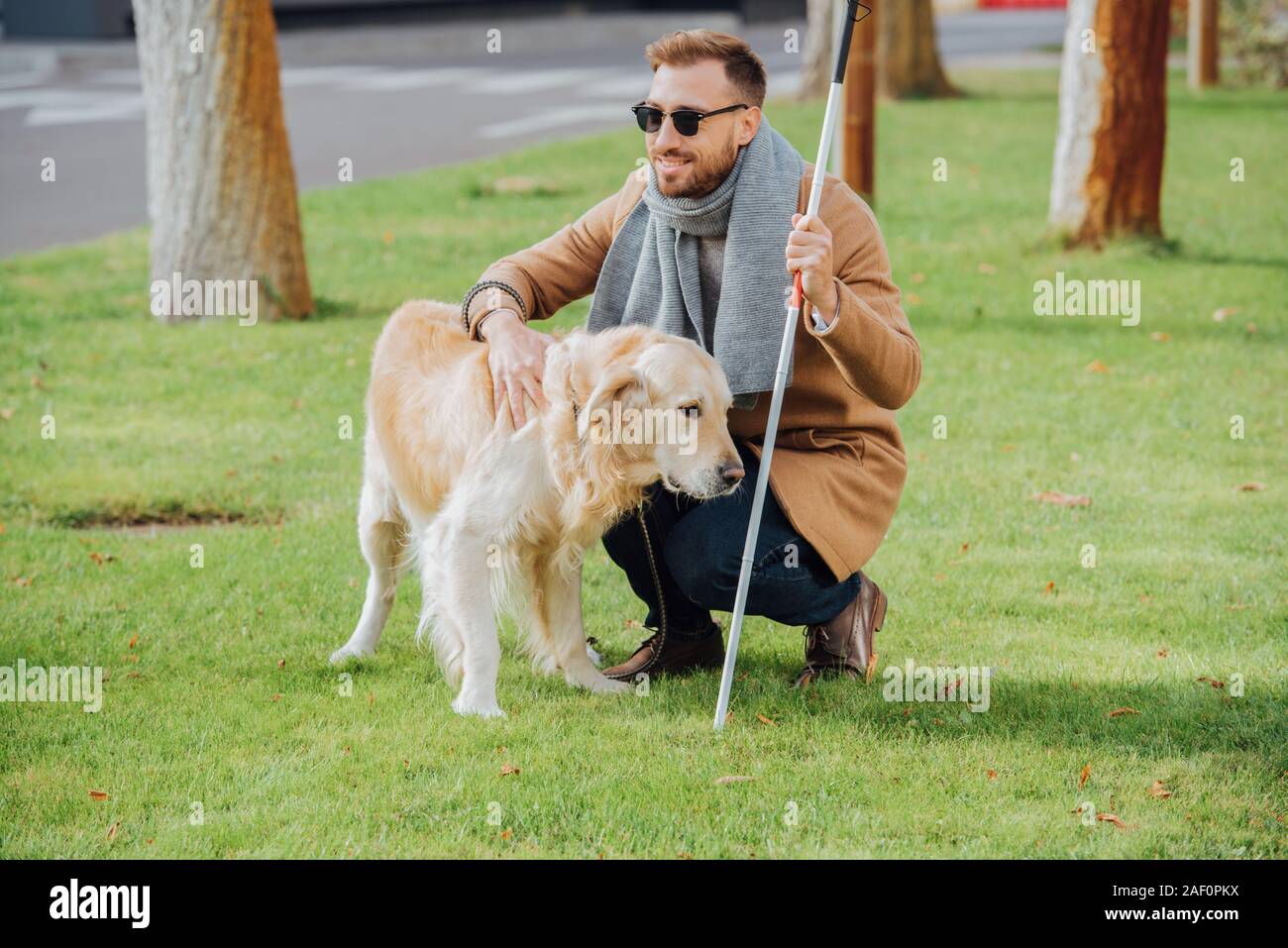 Lächelnd blinder Mann mit Stock Streichelzoo Hund auf Rasen Stockfoto