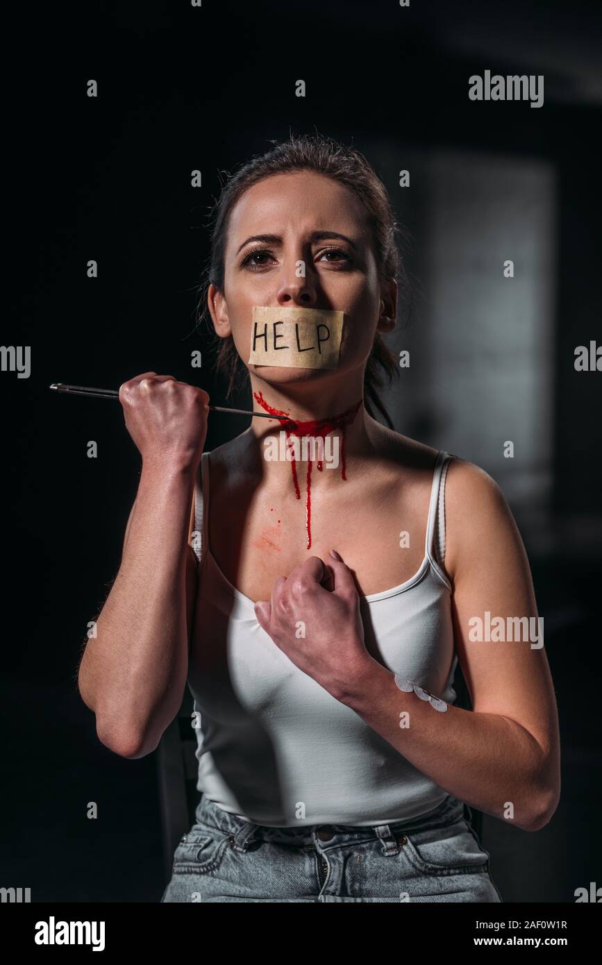 Frau mit Wort Hilfe auf Klebeband auf den Mund Selbstmord zu begehen, indem die Kehle mit Rasiermesser auf dunklem Hintergrund fixiert Stockfoto