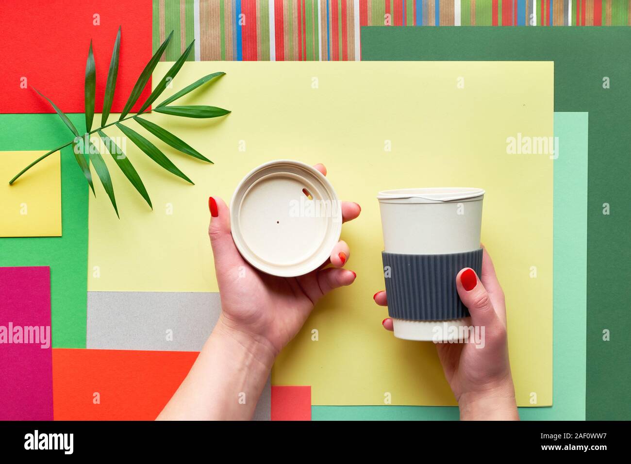 Bambus Kaffee Tasse (Cup oder Reisebecher) mit Deckel in weibliche Hände auf abstrakte geometrische multicolor Rechteck Papier Hintergrund mit Palm Leaf. Creati Stockfoto