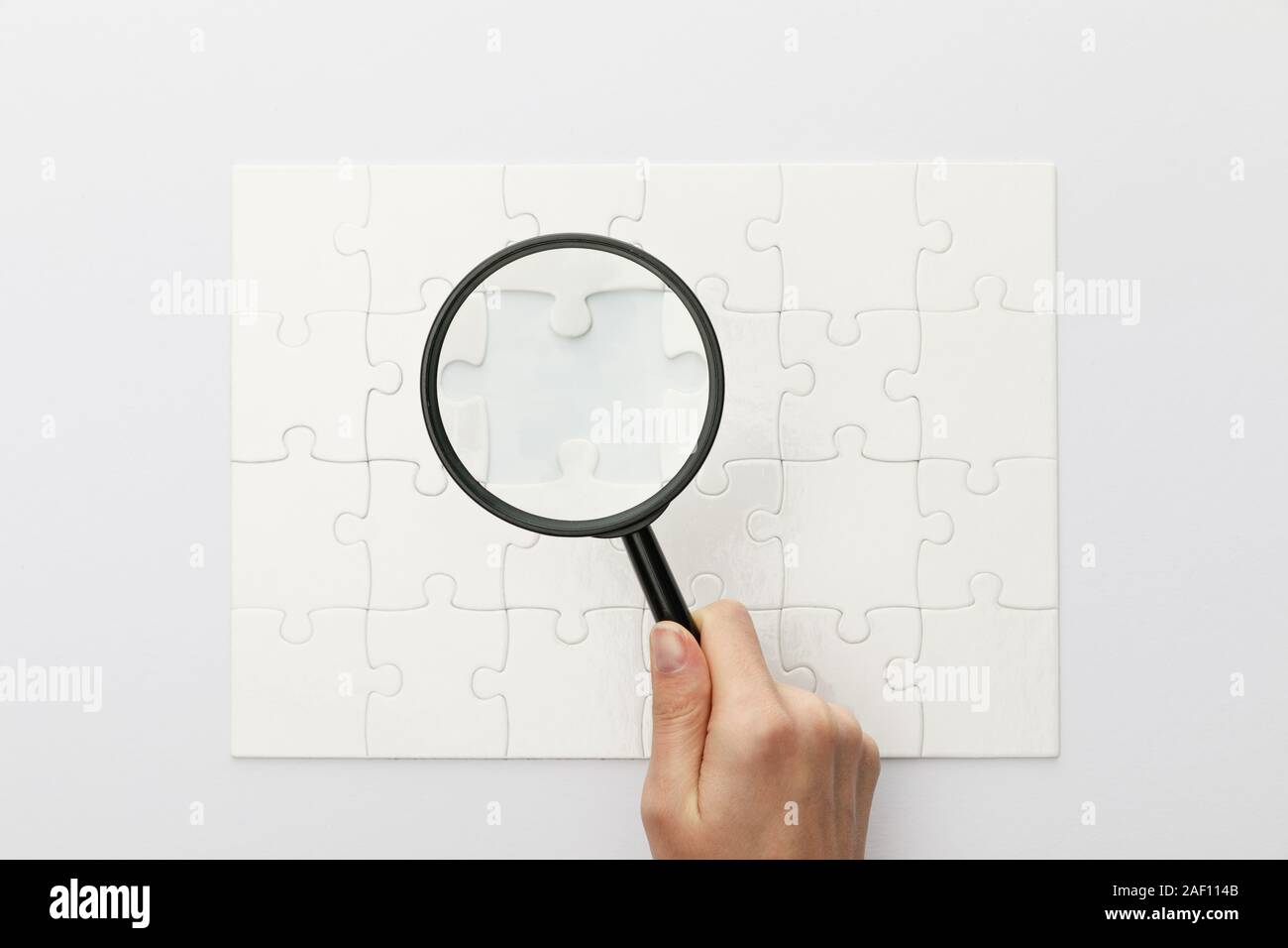 7/8-Ansicht von Frau mit Lupe unter Puzzle auf weißem Hintergrund Stockfoto