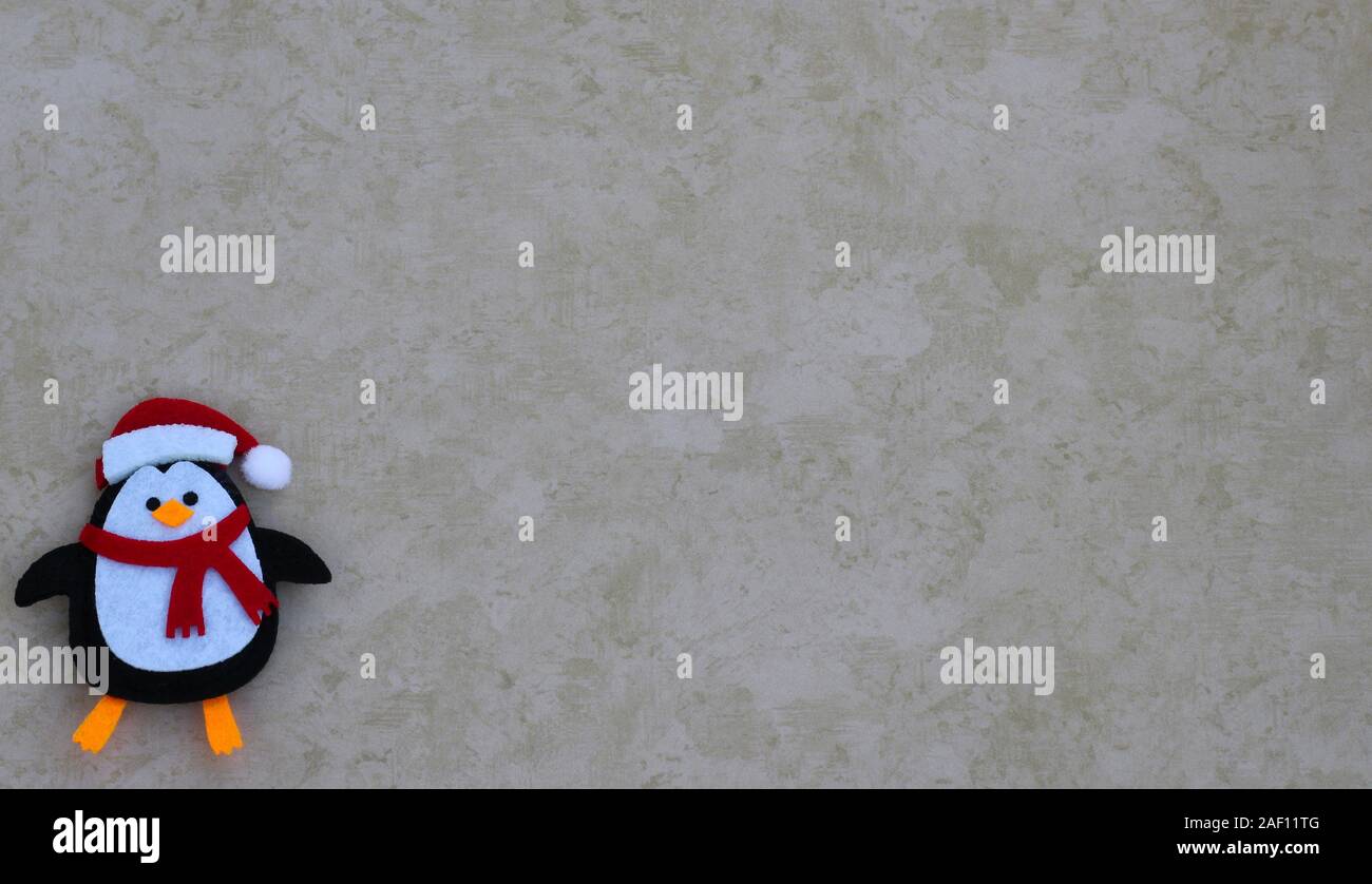 Urlaub in Handarbeit Filz gestaltete Pinguin trägt einen Schal und Santa Claus Hut auf einem tan Hintergrund mit Kopie Raum Stockfoto