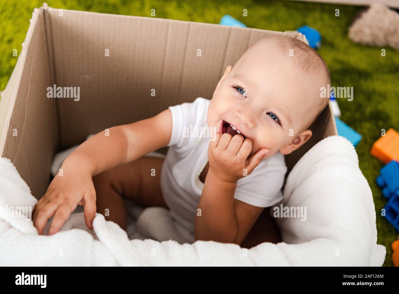 Nette blauäugige Kind sitzen und Lächeln, in Karton mit Decke Stockfoto