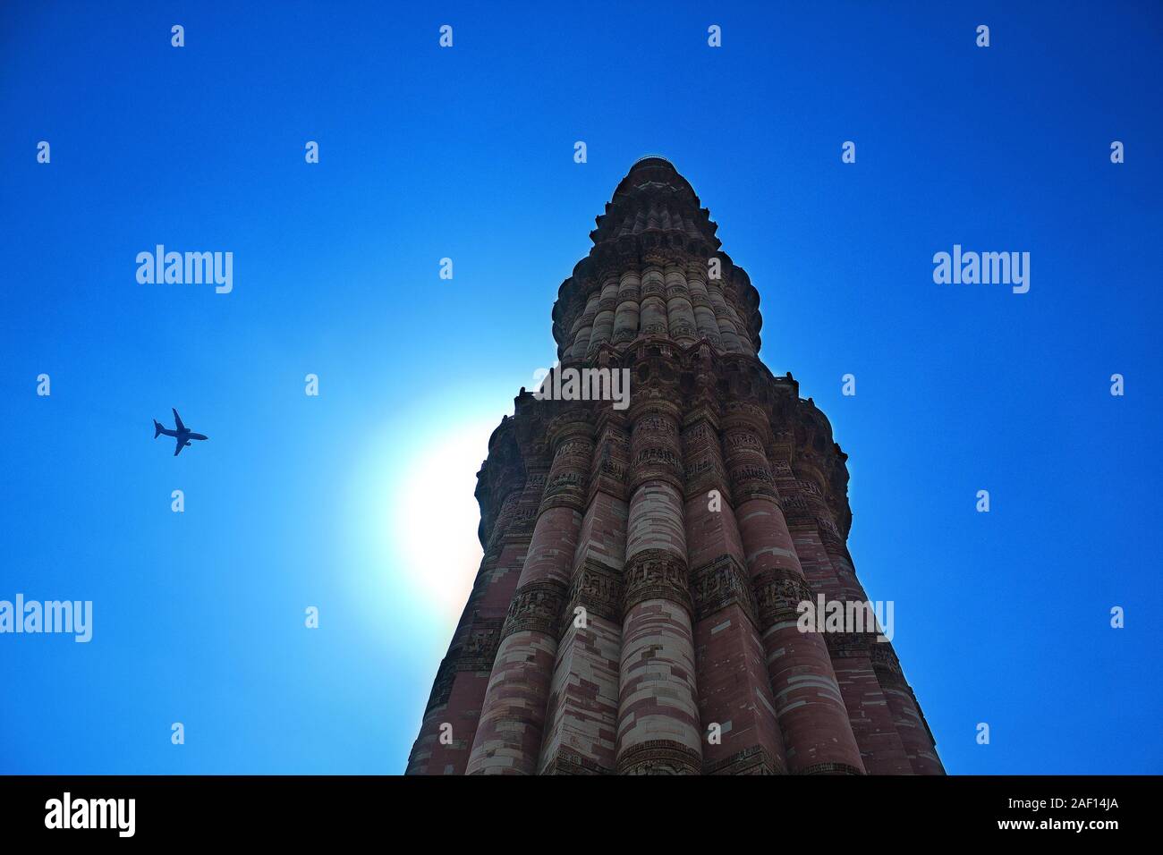 Qutb Minar gegen einem azurblauen Himmel mit einem entgegenkommenden Flugzeug. In Delhi, Indien Stockfoto