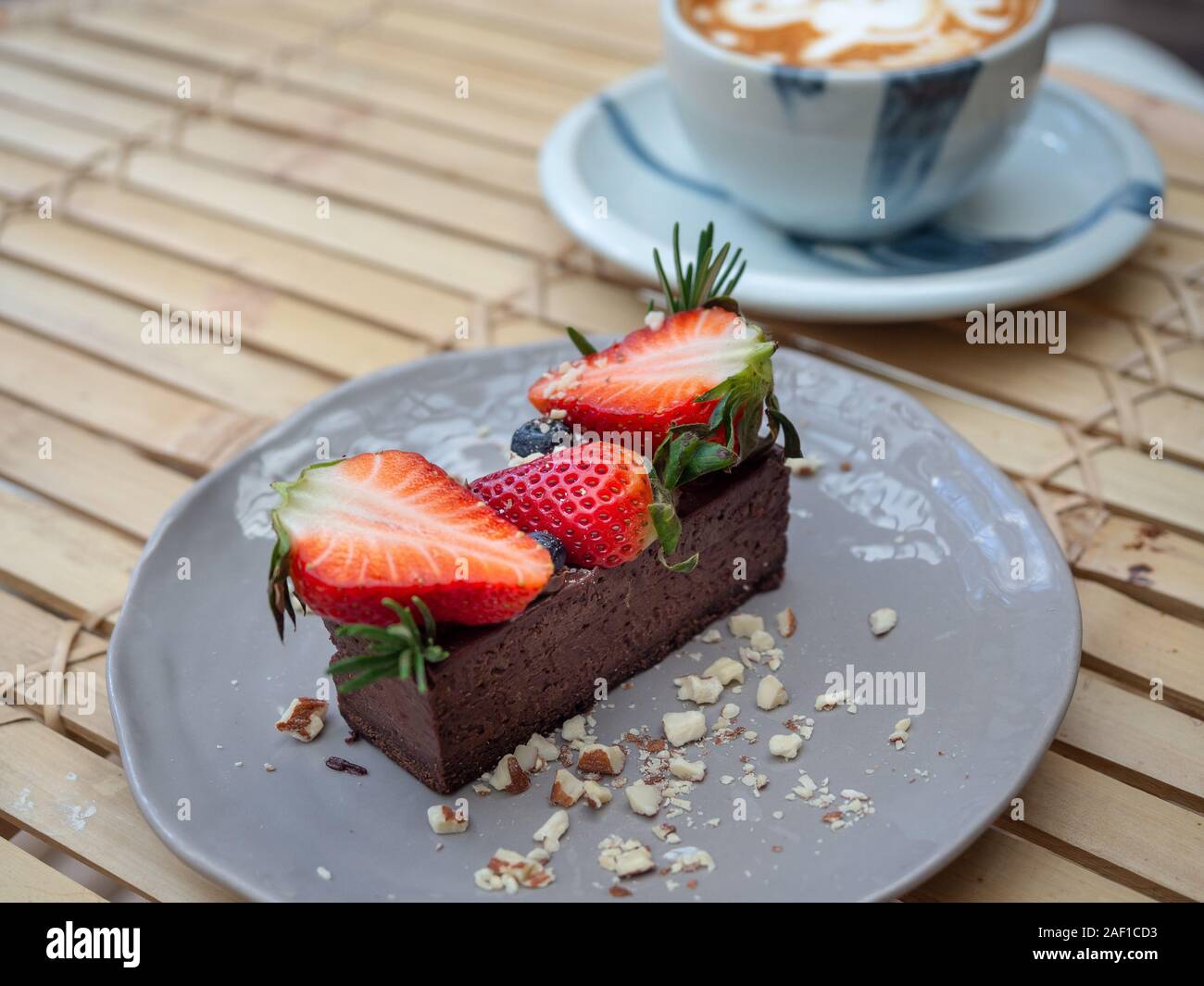 Köstliche Schokolade Torte mit Erdbeeren und Beeren auf Graue Keramik Schüssel mit heißem Kaffee Tasse auf Bambus Tisch lagen. Stockfoto