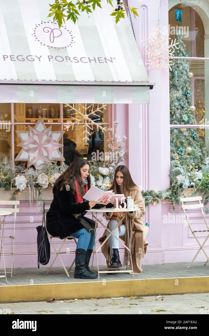 Junge Frauen an einem Tisch draußen Peggy porschen Cake Shop Sitzung im Dezember. Belgravia, London, England Stockfoto