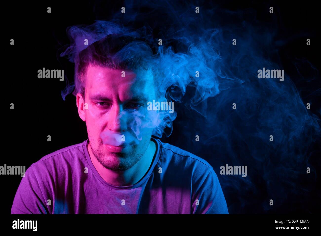 Nahaufnahme, Portrt des Gesicht von einem erwachsenen Mann atmet Blau  toxischen Rauch beim Rauchen E-Zigarette und vape beleuchtet mit rosa  farbiges Licht Stockfotografie - Alamy