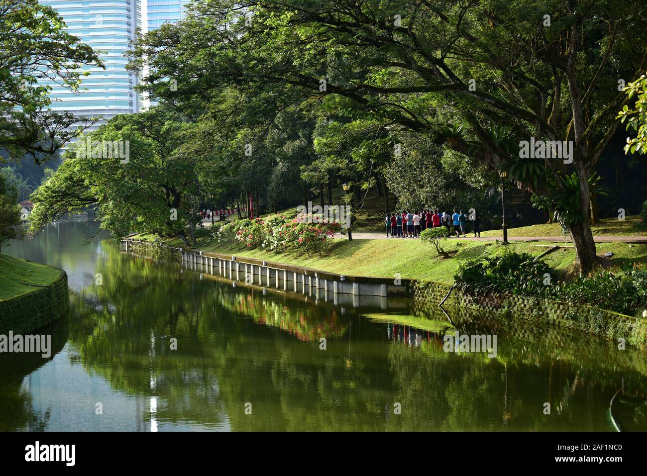 Gruppe von Menschen im Botanischen Garten läuft mit Wolkenkratzern im Hintergrund. Kuala Lumpur Stockfoto