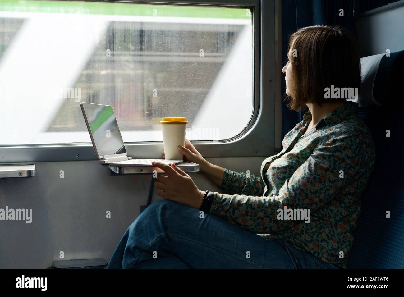 Eine Frau sitzt am Fenster einer S-Bahn mit einem Laptop und Kaffee Tasse Stockfoto