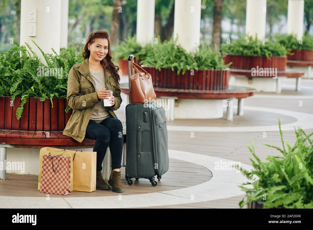 Portrait von lächelnden vietnamesische Frau sitzt auf der Bank am Bahnhof und trinken Kaffee zum Mitnehmen Stockfoto