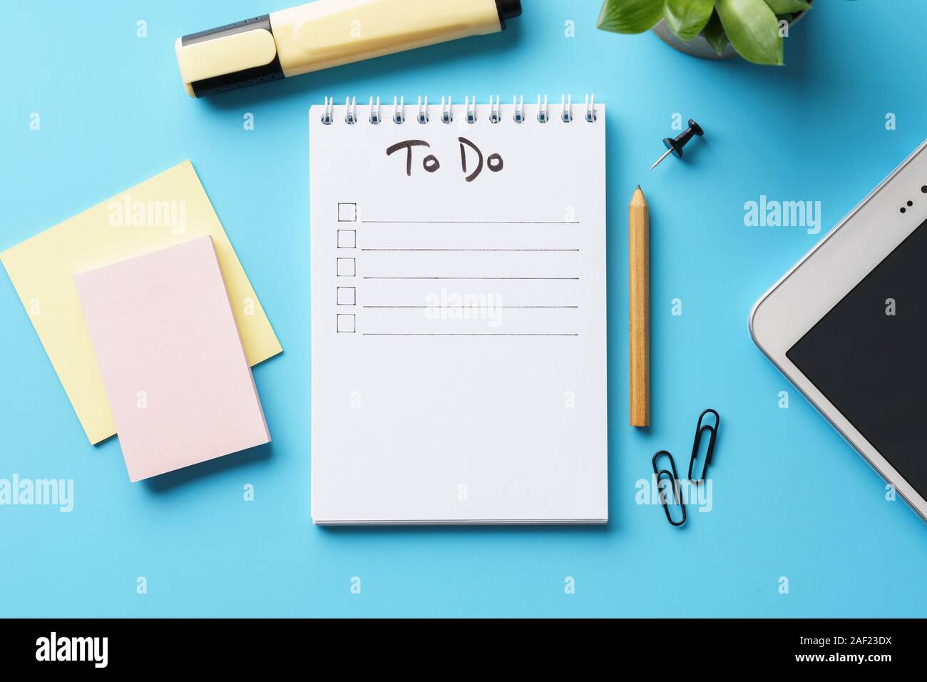 Ein Notebook mit Zu-Liste auf einem blauen Schreibtisch mit Briefpapier und eine Topfpflanze. Flach. Kopieren Sie Platz. Stockfoto