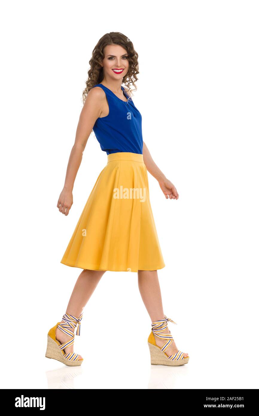 Wandern schöne junge Frau in gelb Rock, blau oben und Keil Schuhe. Von der Seite. Volle Länge studio Schuß auf weißen isoliert. Stockfoto