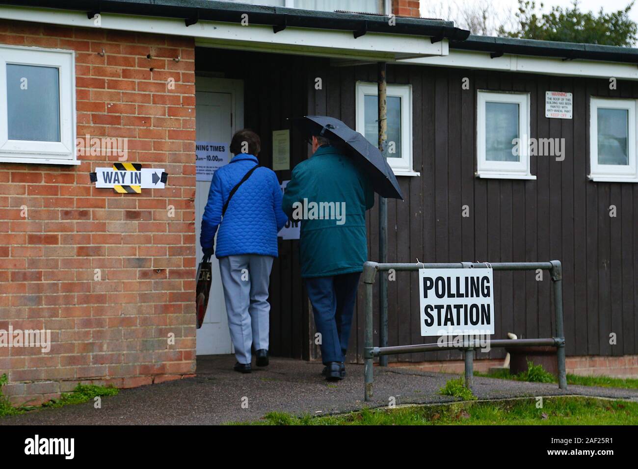 Ashford, Kent, Großbritannien. 12. Dezember, 2019. Auf einem nassen und miserablen Tag Briten gehen zu den Abstimmungen. Ein älteres Paar Spaziergang im strömenden Regen mit einem Regenschirm in der Hand auf das lokale Dorf Halle Wahllokal, in dem kleinen Dorf Hamstreet außerhalb von Ashford, Kent. © Paul Lawrenson 2019, Foto: Paul Lawrenson/Alamy leben Nachrichten Stockfoto