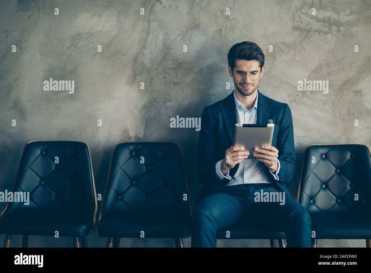 Portrait von fokussierter Unternehmer warten, Treffen mit Partnern sitzen auf Stuhl Arbeit auf Tablet lesen Sie die Nachrichten tragen moderne blaue Blazer Hose Stockfoto