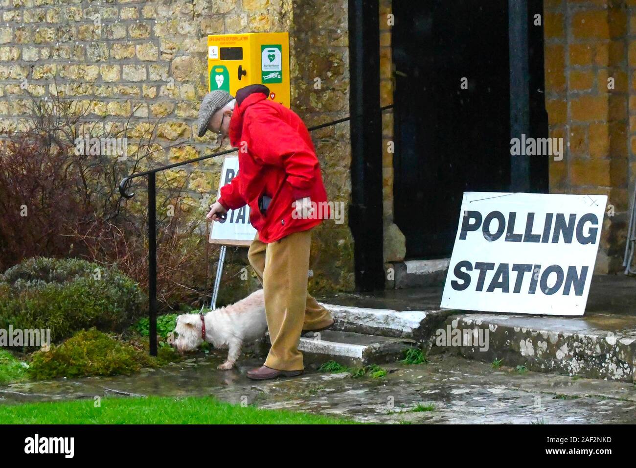 Walditch, Dorset, Großbritannien. 12. Dezember 2019. Ein Mann, der eine wasserdichte Jacke hinterlässt mit seinem Hund im Regen nach der Abstimmung im Wahllokal an Walditch in Dorset auf einem nassen allgemeinen Wahltag. Foto: Graham Jagd-/Alamy leben Nachrichten Stockfoto