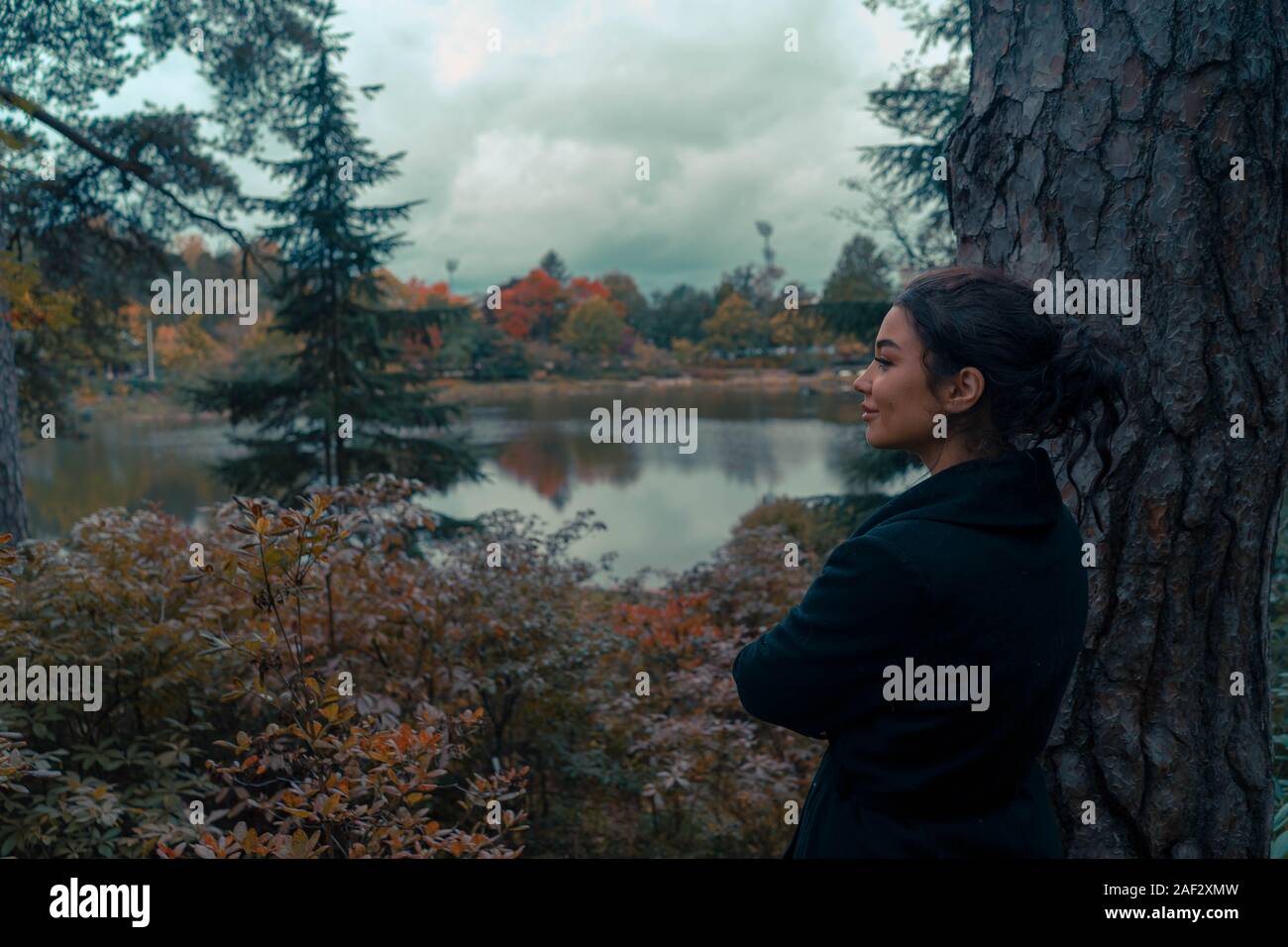 Junge attraktive Frau mit Blick auf Teich in den schönen Park in Finnland und lächelnd. Konzept der Harmonie und Einheit mit der Natur Stockfoto
