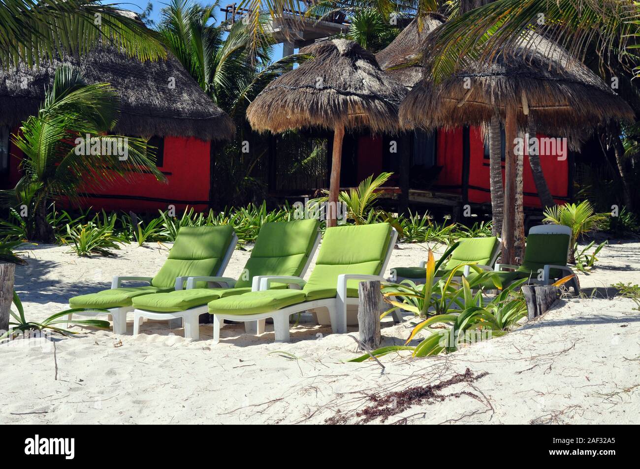 Grüne Liegen in den Sand mit zwei Orange Beach Hütten und strohgedeckten Sonnenschirmen. Stockfoto