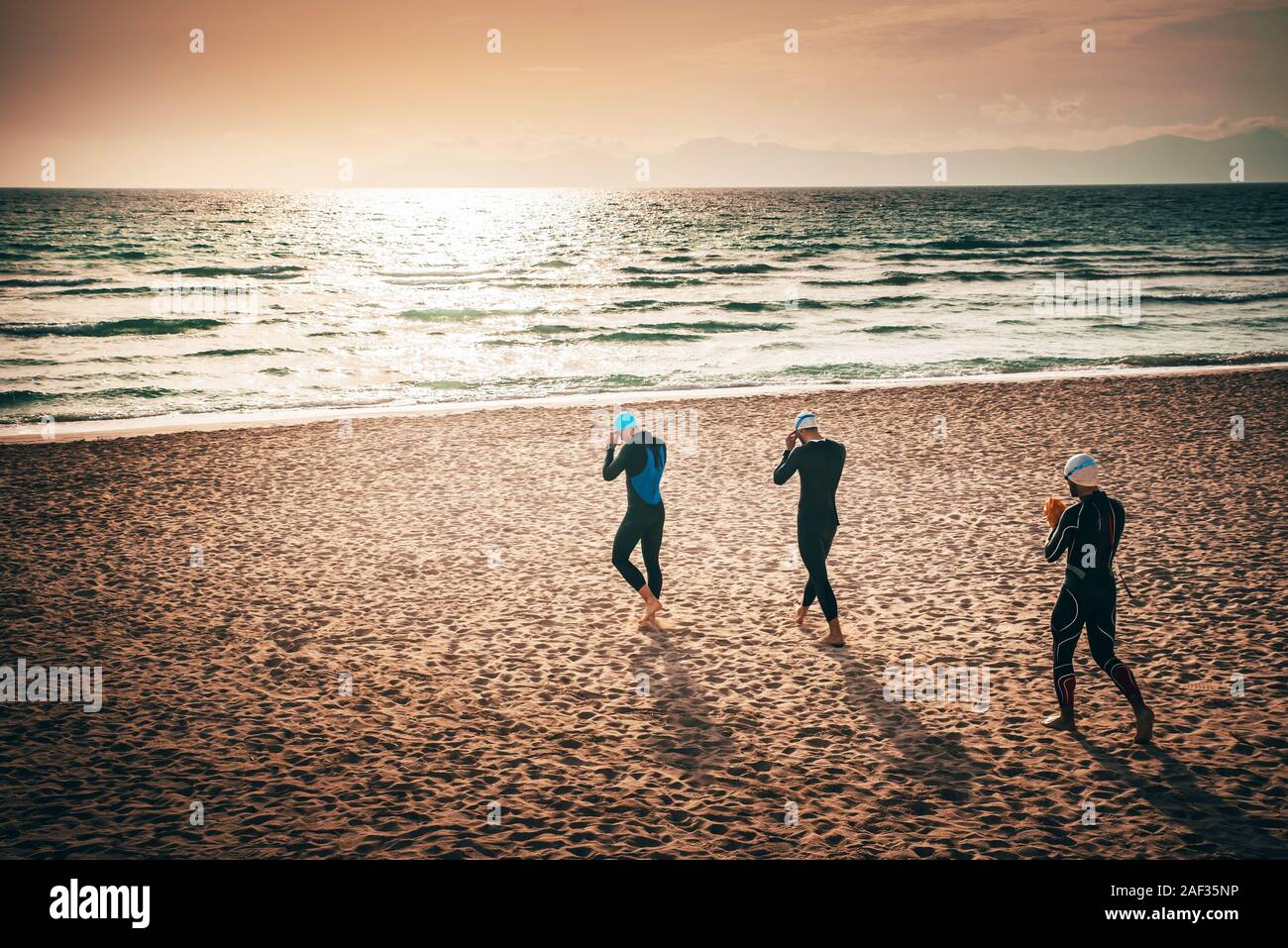 Drei triathlon die Teilnehmer zu Fuß am Strand vor dem Schwimmen Training. Mallorca, Spanien Stockfoto