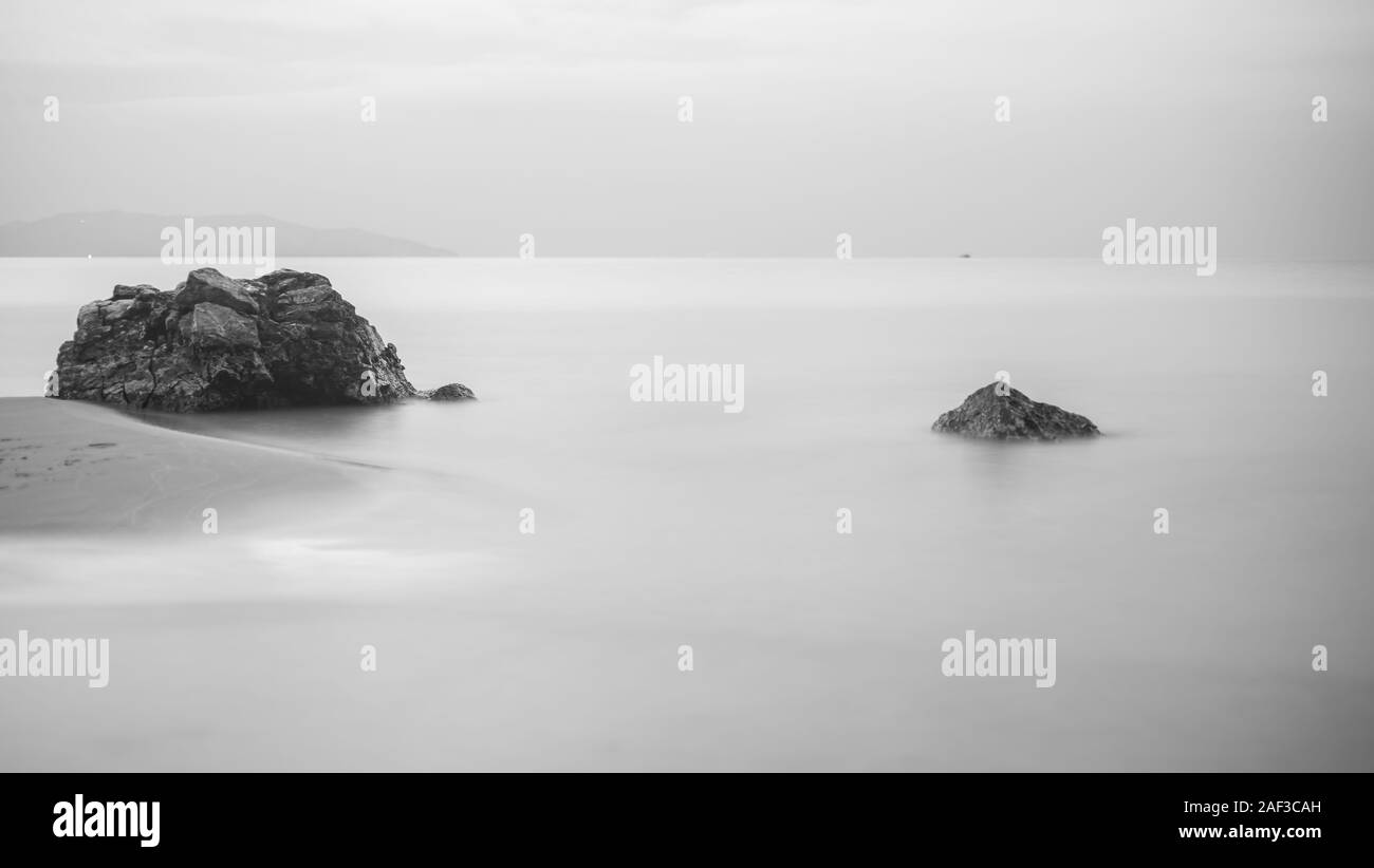 Schwarze und weiße Feder-förmige Bild von Felsen und Wellen auf dem Meer. Soft Focus wegen der langen Belichtungszeit. Künstlerische Bild von schwarzen Felsen und Meer auf der Stockfoto