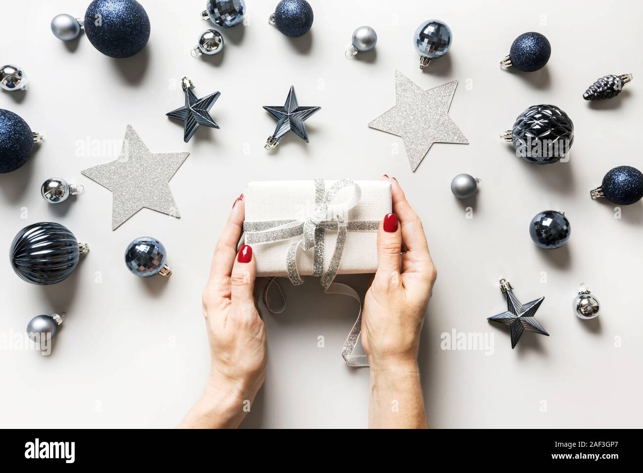 Weihnachten Zusammensetzung der klassischen blauen Kugeln und Geschenkbox in womans Hand auf Grau. Ansicht von oben. Weihnachten. Urlaub Grußkarte. Trendfarbe des Jahres 2020. Stockfoto