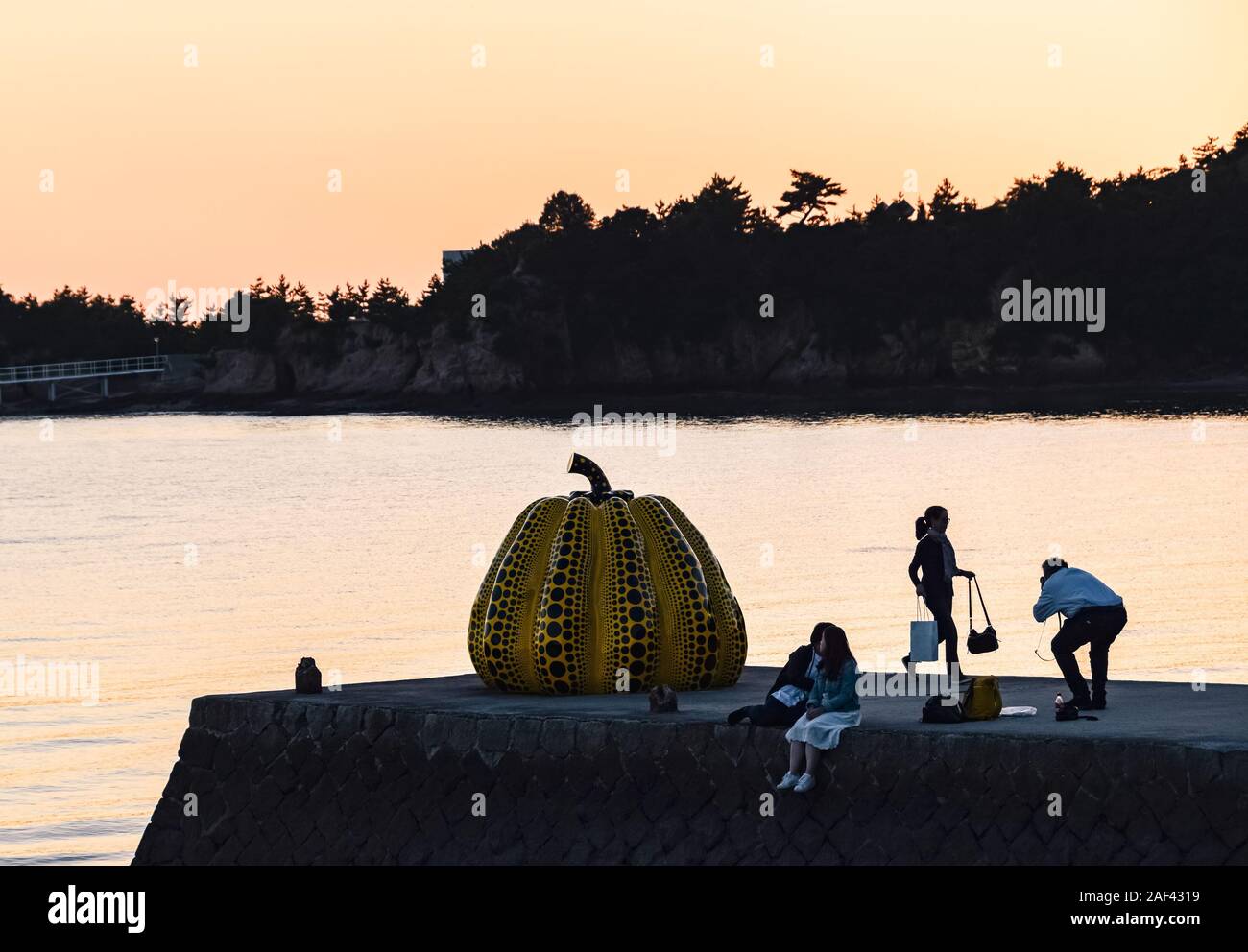 Touristen Aufnehmen von Fotos mit Yayoi Kusama Giant's gelber Kürbis Skulptur bei Sonnenuntergang in Naoshima, Japan. Stockfoto