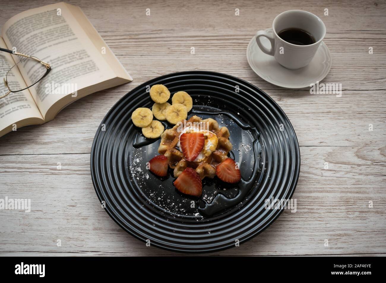 Leckere Waffeln mit Früchten auf einem Tisch mit einem Kaffee und einem Buch Stockfoto