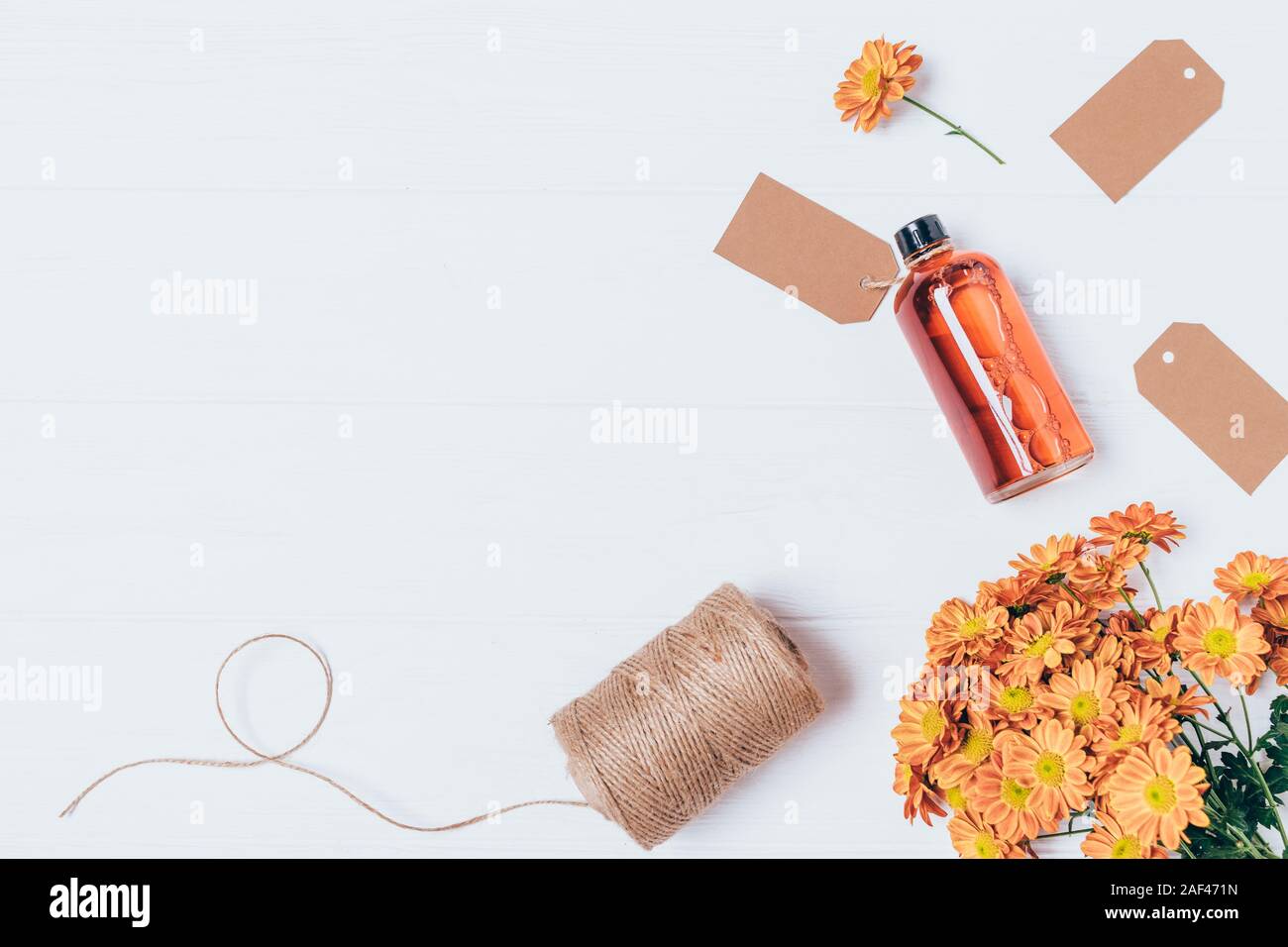 Flach handgemachte Kosmetik lotion Flasche neben Strauß mit frischen Blumen, Jute Seil und Tags auf weiße Holztisch. Stockfoto