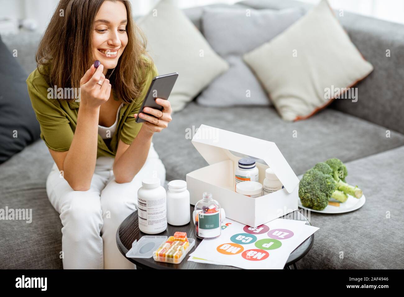 Frau Einnahme von Nahrungsergänzung in Form von Pillen, während mit Smart Phone, zu Hause zu sitzen. Konzept der individuellen online Auswahl von Nahrungsergänzungsmitteln. Präventive Medizin Stockfoto